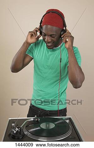 Stock Photo - A DJ listening to headphones in front of turntable. Fotosearch