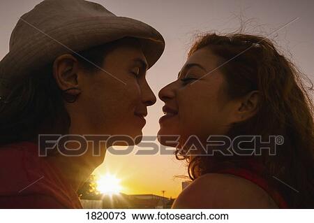 Affectionate couple kissing with sunset in background View Large Photo Image Stock Image - Affectionate couple kissing with sunset in background. Fotosearch