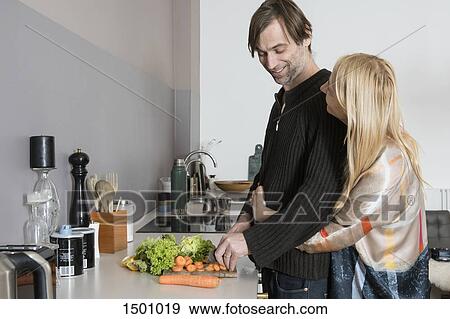 Stock Photo - Affectionate mature couple cooking food together in kitchen. Fotosearch