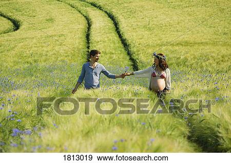 Affectionate pregnant couple holding hands, walking in sunny, idyllic rural green field View Large Photo Image Stock Photo - Affectionate pregnant couple holding hands, walking in sunny, idyllic rural green field. Fotosearch