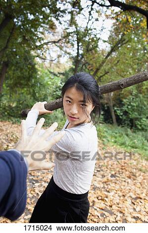 Picture - Aggressive woman holding stick in front of hand at park. Fotosearch