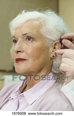 Audiologist assisting senior woman in inserting hearing aid at clinic View Large Photo Image Stock Photo - Audiologist assisting senior woman in inserting hearing aid at clinic. Fotosearch