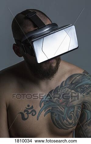 Picture - Bare chested man with tattoos using virtual reality simulator. Fotosearch