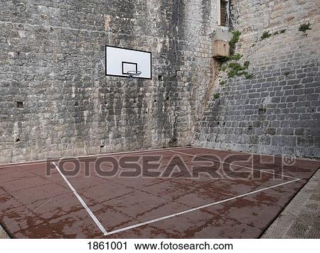 Stock Image - Basketball court and hoop in stone courtyard. Fotosearch