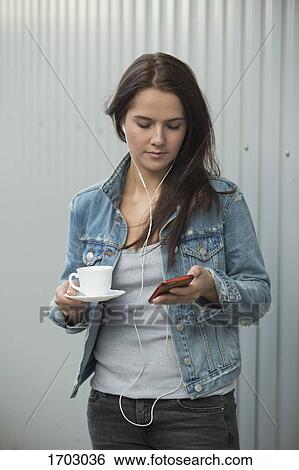 Beautiful woman using mobile phone while holding coffee cup against metallic wall View Large Photo Image Stock Photograph - Beautiful woman using mobile phone while holding coffee cup against metallic wall. Fotosearch