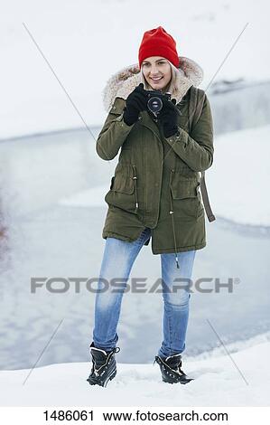 Stock Image - Beautiful young woman photographing through camera during winter. Fotosearch