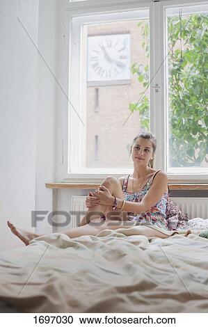 Beautiful young woman sitting on bed against window at home View Large Photo Image Stock Image - Beautiful young woman sitting on bed against window at home. Fotosearch