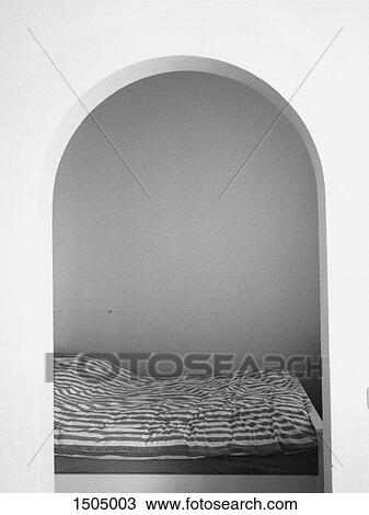 Stock Image - Bed and room seen through an arch. Fotosearch