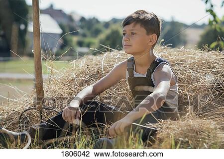 Boy in overalls sitting in hay on sunny farm View Large Photo Image Stock Image - Boy in overalls sitting in hay on sunny farm. Fotosearch