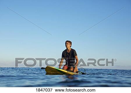 Boy kneeling on paddle board on blue ocean View Large Photo Image Stock Photo - Boy kneeling on paddle board on blue ocean. Fotosearch