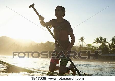 Boy kneeling on paddle board on sunny sunset ocean View Large Photo Image Stock Photo - Boy kneeling on paddle board on sunny sunset ocean. Fotosearch