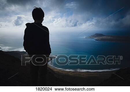 Boy looking at scenic ocean bay view with storm clouds overhead, Lanzarote, Canary Islands, Spain View Large Photo Image Picture - Boy looking at scenic ocean bay view with storm clouds overhead, Lanzarote, Canary Islands, Spain. Fotosearch