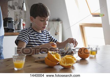 Picture - Boy making orange juice at table in house. Fotosearch