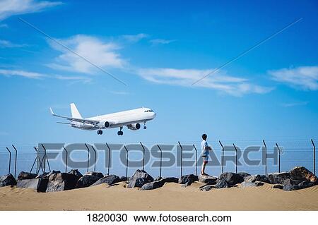 Boy on beach watching airplane flying low in blue sky near Lanzarote Airport, Spain View Large Photo Image Stock Image - Boy on beach watching airplane flying low in blue sky near Lanzarote Airport, Spain. Fotosearch