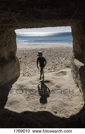 Boy on sunny ocean beach walking into cave View Large Photo Image Stock Image - Boy on sunny ocean beach walking into cave. Fotosearch