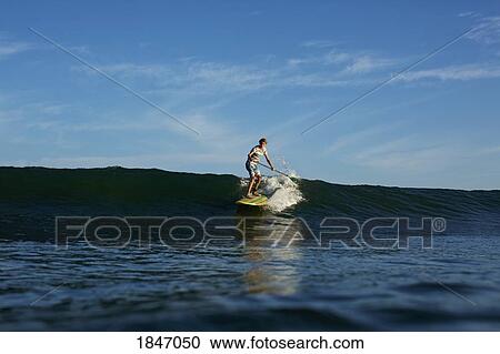 Boy paddle boarder riding sunny, blue ocean wave View Large Photo Image Stock Image - Boy paddle boarder riding sunny, blue ocean wave. Fotosearch