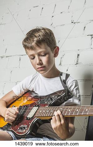 Stock Photo - Boy playing guitar against wall at home. Fotosearch