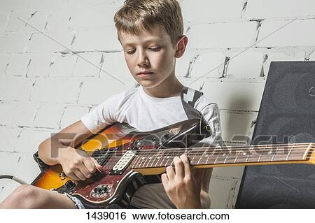 Boy playing guitar while sitting at home View Large Photo Image Stock Photograph - Boy playing guitar while sitting at home. Fotosearch