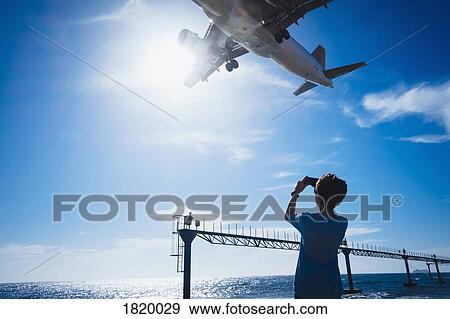 Stock Photo - Boy with camera phone photographing airplane flying low overhead near Lanzarote Airport. Fotosearch