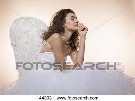 Bride with eyes closed wearing angel wings while sitting against colored background View Large Photo Image Stock Image - Bride with eyes closed wearing angel wings while sitting against colored background. Fotosearch