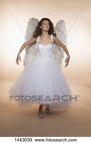 Stock Photo - Bride with eyes closed wearing angel wings while standing against colored background. Fotosearch