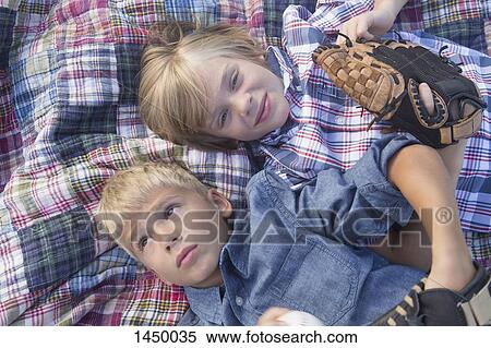 Stock Photography - Brothers wearing baseball gloves while relaxing on sheet in yard. Fotosearch