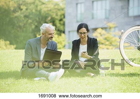 Business colleagues discussing while sitting on grass field View Large Photo Image Stock Photo - Business colleagues discussing while sitting on grass field. Fotosearch