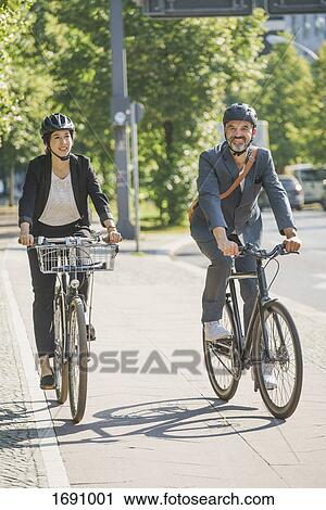 Business colleagues riding bicycle on road in city during sunny day View Large Photo Image Stock Image - Business colleagues riding bicycle on road in city during sunny day. Fotosearch