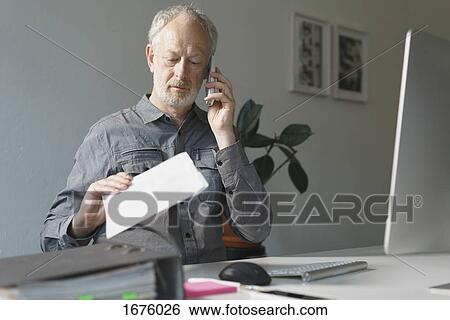 Businessman talking through mobile phone while working at desk in office View Large Photo Image Stock Photograph - Businessman talking through mobile phone while working at desk in office. Fotosearch