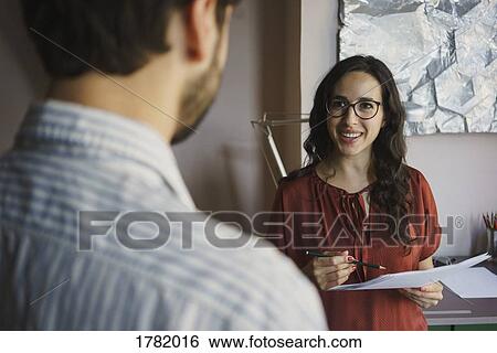 Businesswoman with paperwork talking to colleague in office View Large Photo Image Stock Photograph - Businesswoman with paperwork talking to colleague in office. Fotosearch