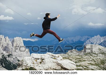 Stock Image - Carefree boy jumping over rocks on mountain, Drei Zinnen Nature Park, South Tyrol, Italy. Fotosearch