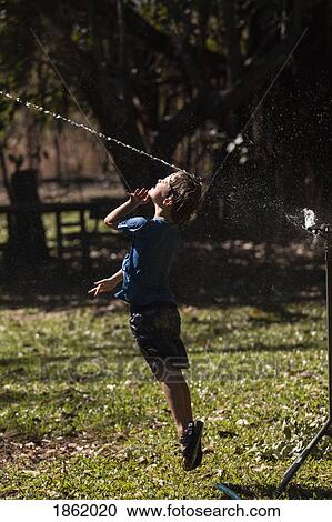 Carefree boy jumping up into sprinkler in sunny back yard View Large Photo Image Stock Image - Carefree boy jumping up into sprinkler in sunny back yard. Fotosearch