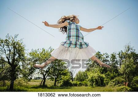 Stock Image - Carefree girl in dress jumping for joy in sunny backyard. Fotosearch