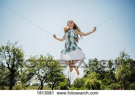Stock Image - Carefree girl in dress jumping for joy in sunny backyard. Fotosearch