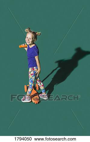 Carefree girl riding scooter against green background View Large Photo Image Stock Image - Carefree girl riding scooter against green background. Fotosearch