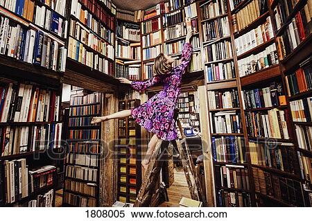 Carefree woman on ladder reaching for book in library View Large Photo Image Stock Photography - Carefree woman on ladder reaching for book in library. Fotosearch