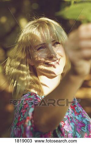 Stock Image - Carefree woman reaching for leaf. Fotosearch