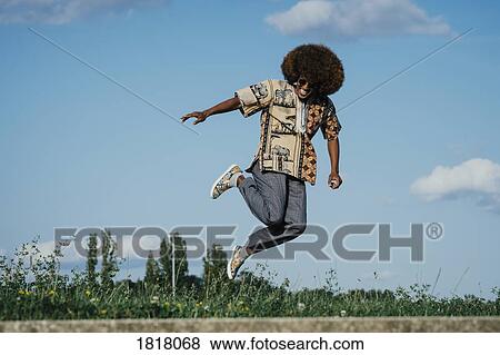 Carefree young man with afro jumping for joy View Large Photo Image Stock Photo - Carefree young man with afro jumping for joy. Fotosearch
