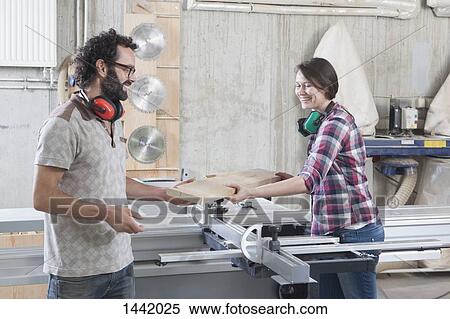 Stock Photography - Carpenters laughing while using sliding table saw in workshop. Fotosearch