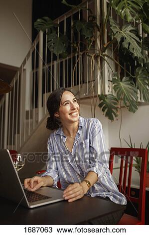 Cheerful young woman looking away while using laptop at home View Large Photo Image Stock Image - Cheerful young woman looking away while using laptop at home. Fotosearch