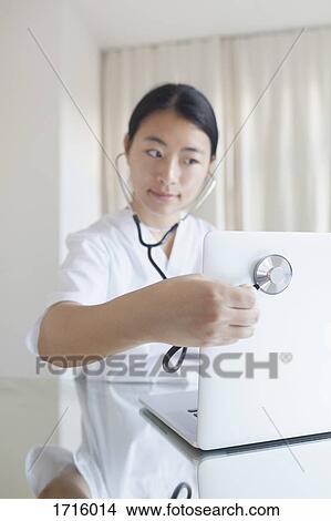 Close-up of doctor examining laptop with stethoscope at desk in clinic View Large Photo Image Picture - Close-up of doctor examining laptop with stethoscope at desk in clinic. Fotosearch