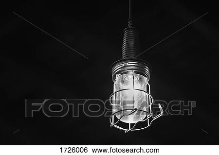 Stock Photograph - Close-up of illuminated light bulb hanging in dark room. Fotosearch