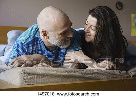 Stock Photo - Close-up of mature couple lying on bed at home. Fotosearch