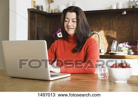 Stock Image - Close-up of mature woman using laptop on table at home. Fotosearch