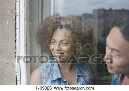 Stock Image - Close-up of smiling couple looking through glass window. Fotosearch