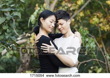 Picture - Close-up of smiling lesbian couple embracing against plants at park. Fotosearch