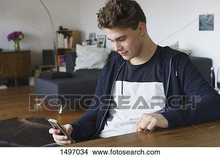 Close-up of teenage boy using smart phone while sitting by table at home View Large Photo Image Picture - Close-up of teenage boy using smart phone while sitting by table at home. Fotosearch