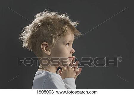 Stock Image - Close-up of thoughtful boy with hand on chin against gray background. Fotosearch