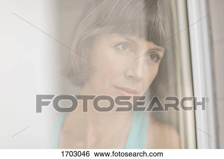 Stock Photograph - Close-up of thoughtful mature woman seen from window glass. Fotosearch