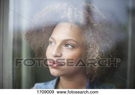 Stock Photo - Close-up of thoughtful woman with curly hair seen through glass window. Fotosearch